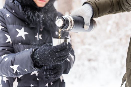 Thermos and cold season concept - A woman pours a hot drink. Couple on a winter holiday.