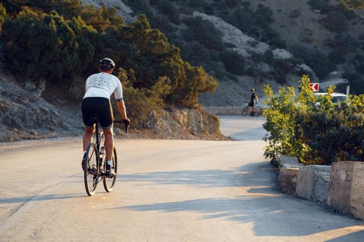 Man cyclist pedaling on a road bike outdoors in sun set at coastal road