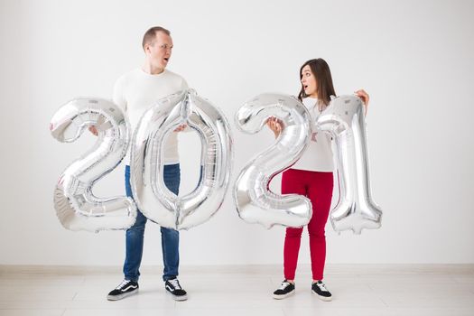 New 2021 Year is coming concept - Happy young man and woman are holding silver colored numbers indoors