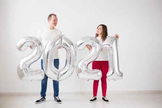 New 2021 Year is coming concept - Happy young man and woman are holding silver colored numbers indoors
