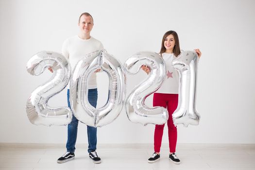 New 2021 Year is coming concept - Happy young man and woman are holding silver colored numbers indoors