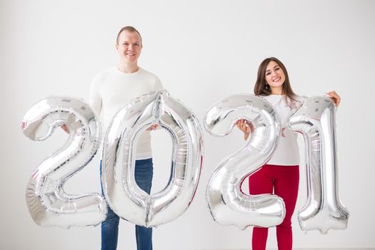 New 2021 Year is coming concept - Happy young man and woman are holding silver colored numbers indoors