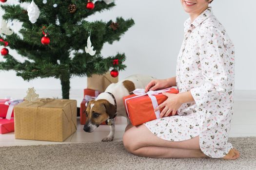 Happy young woman with lovely dog opening present box under christmas tree.