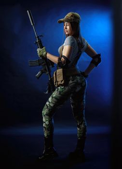 the woman in a military airsoft uniform in a vest with an American automatic rifle on a dark background
