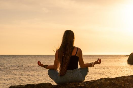 Young woman in swimsuit with long hair practicing stretching outdoors on yoga mat by the sea on a sunny day. Women's yoga fitness pilates routine. Healthy lifestyle, harmony and meditation concept.