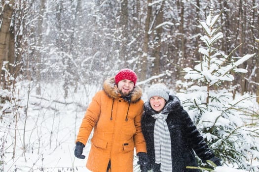 Love, season, friendship and people concept - happy young man and woman having fun and playing with snow in winter forest.