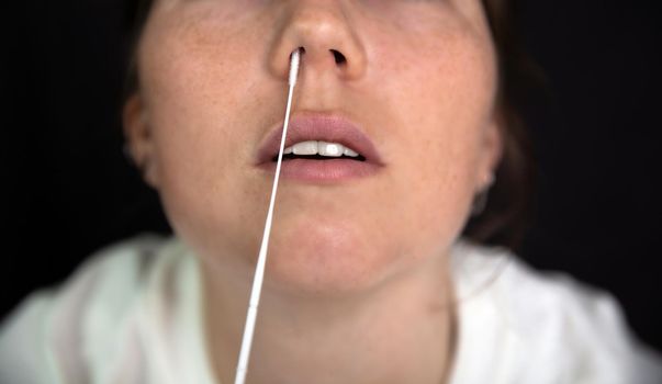 Young woman taking a Covid-19 SARS-CoV-2 test during Corona pandemic on dark black background, quick home test coronavirus closeup nose swab