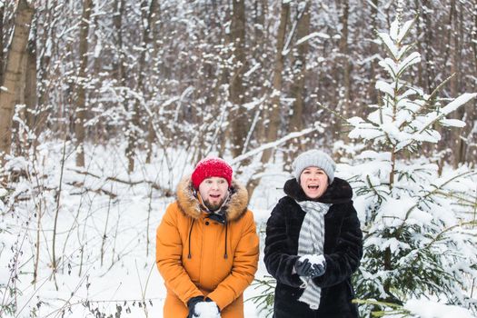 Love, season, friendship and people concept - happy young man and woman having fun and playing with snow in winter forest.