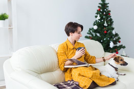Woman reads book in front of Christmas tree with dog jack russell terrier. Christmas, holidays and pet concept.