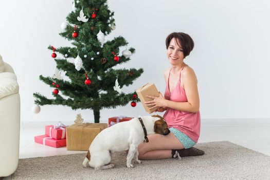 Happy woman with dog opening Christmas gifts. Christmas tree with presents under it. Decorated living room.