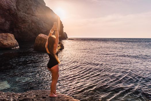 Young woman in swimsuit with long hair practicing stretching outdoors on yoga mat by the sea on a sunny day. Women's yoga fitness pilates routine. Healthy lifestyle, harmony and meditation concept.