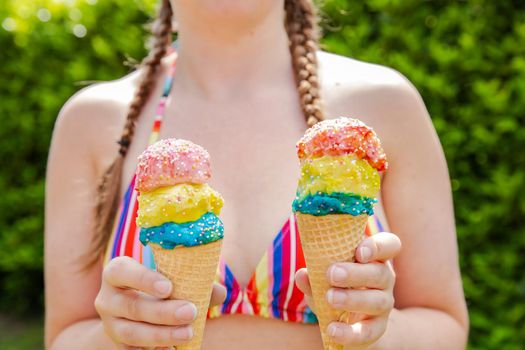 Beautiful girl holding two colorful ice cream with sprinkles wearing a rainbow colored swimsuit in the summer, pink sunglasses and braids happy vacation,holidays concept sunshine