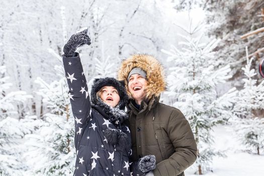 Technologies and relationship concept - Happy smiling couple taking a selfie in a winter forest outside.