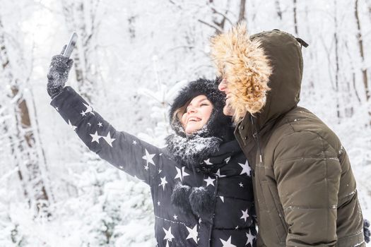 Season, love, technology and leisure concept - happy couple taking selfie by smartphone over winter.