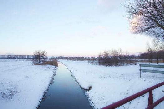 Beautiful winter landscape at sunset with fog and snow covering farmland and river in the Netherlands beautiful colors in nature winter