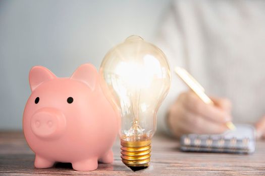 Shining lightbulb and pink piggy bank, business person writing Financial ideas,creative savings,investment budget concept copy space closeup