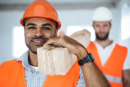 Two young men builders carrying wood planks on construction site, close up photo