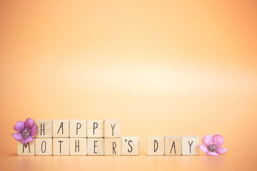 Happy Mother's Day Card. Text Happy mothers Day on bright pastel orange colored background with colorful purple flowers, modern retro design with copy space, Mother,Spring,Greeting card,Holiday concept space for text