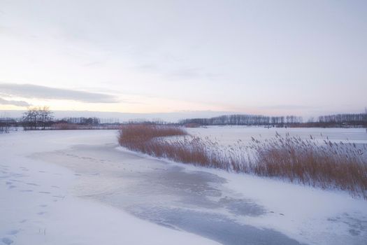Beautiful winter landscape at sunset with fog and snow covering farmland and river in the Netherlands beautiful colors in nature winter