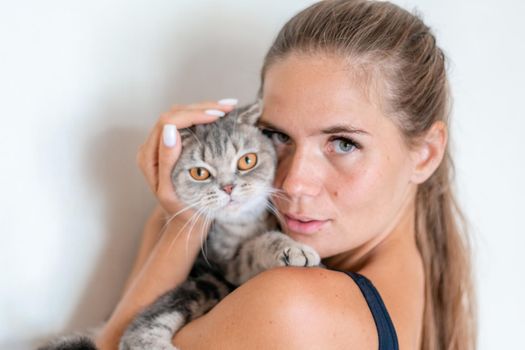 Attractive girl embracing her pet with smile. Indoor portrait of cute ginger woman playing with cat.
