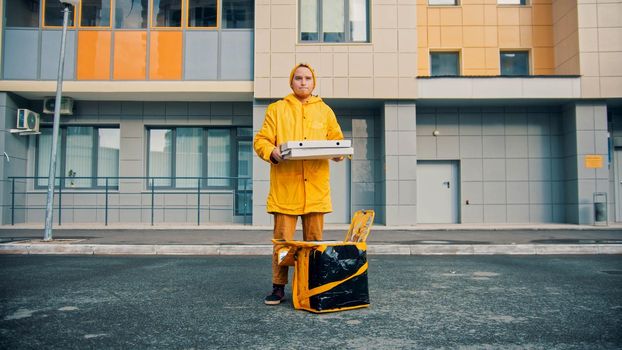 Man courier in yellow clothes delivers food - holding pizza boxes. Mid shot