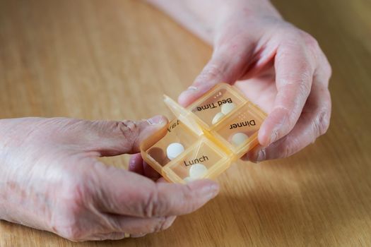 Closeup of an elderly senior woman's hands taking her medication for the week in a pill box on wooden table, business,health concept close up