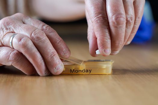 Closeup of an elderly senior woman's hands taking her medication for the week in a pill box on wooden table, business,health concept close up