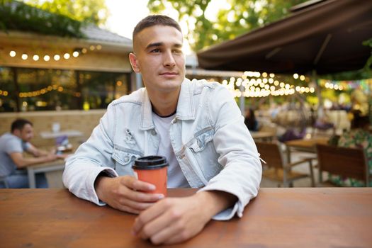 Young man with cup of coffee sitting in outdoor cafe, close up