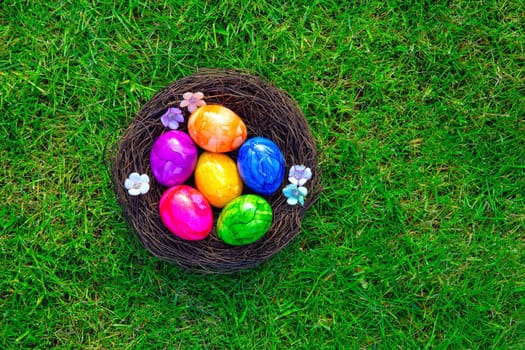 Colorful painted Easter eggs in nest on fresh green grass top view, Happy Easter Holliday concept background with copy space, spring and space for text