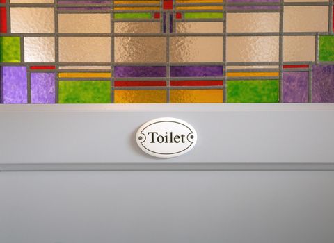 Gray wooden door with Toilet sign text and colorful stained glass in building, closeup background texture modern design colors