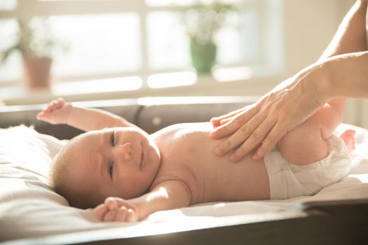 Mother with her hands on her baby lying on a bed. Mid shot