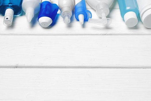 Row of bottles with hand sanitizers, liquid soap and medical preparations on white wooden background
