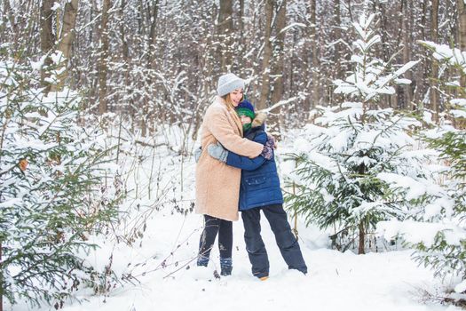 Parenting, fun and season concept - Happy mother and son having fun and playing with snow in winter forest.