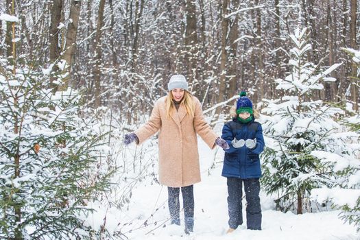 Parenting, fun and season concept - Happy mother and son having fun and playing with snow in winter forest.