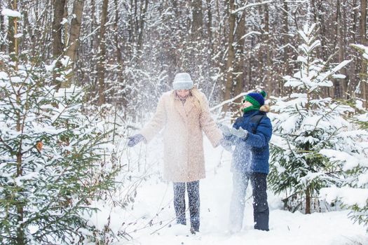 Parenting, fun and season concept - Happy mother and son having fun and playing with snow in winter forest.