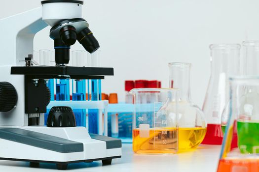 Microscope and colored test tubes on table in laboratory, close up