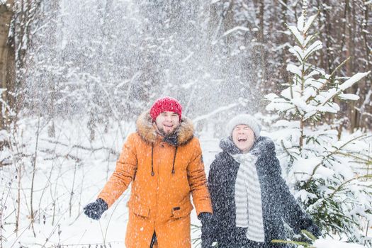 Love, season, friendship and people concept - happy young man and woman having fun and playing with snow in winter forest.