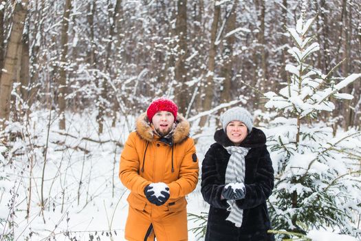 Love, season, friendship and people concept - happy young man and woman having fun and playing with snow in winter forest.