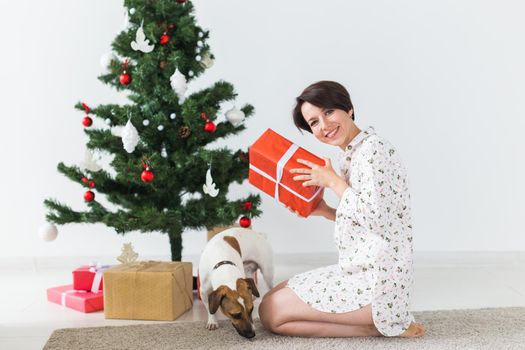 Happy woman with dog opening Christmas gifts. Christmas tree with presents under it. Decorated living room.