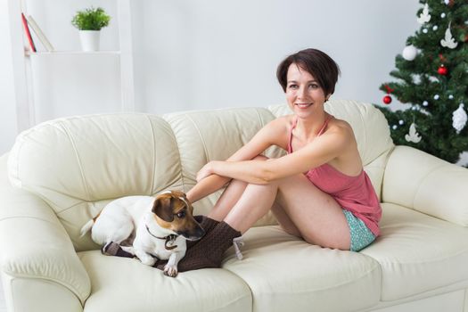 Happy woman with dog. Christmas tree with presents under it. Decorated living room.