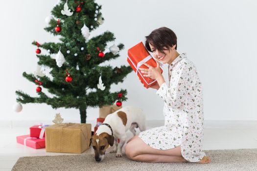 Happy woman with dog opening Christmas gifts. Christmas tree with presents under it. Decorated living room.