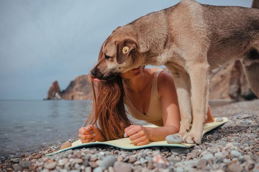 Young woman in swimsuit with long hair practicing stretching outdoors on yoga mat by the sea on a sunny day. Women's yoga fitness pilates routine. Healthy lifestyle, harmony and meditation concept.