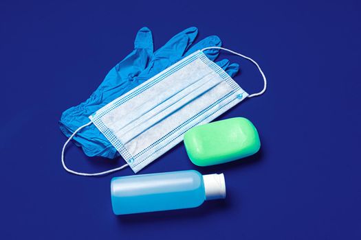 Coronavirus prevention. Facial mask, gloves, soap and sanitizer on blue background close up