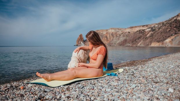 Young woman in swimsuit with long hair practicing stretching outdoors on yoga mat by the sea on a sunny day. Women's yoga fitness pilates routine. Healthy lifestyle, harmony and meditation concept.