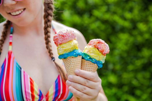 Beautiful girl holding two colorful ice cream with sprinkles wearing a rainbow colored swimsuit in the summer, pink sunglasses and braids happy vacation,holidays concept sunshine