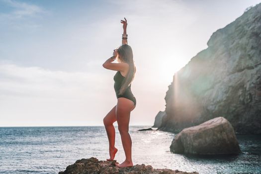 Young woman in swimsuit with long hair practicing stretching outdoors on yoga mat by the sea on a sunny day. Women's yoga fitness pilates routine. Healthy lifestyle, harmony and meditation concept.