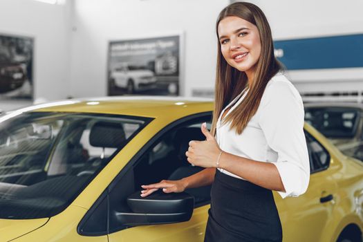 Young woman checking out a new car she is going to buy in car salon