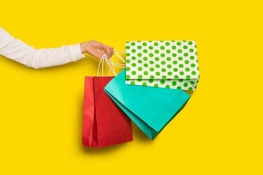 Shopping or sale concept. Female hand holds shopping paper bags isolated on yellow background. Banner