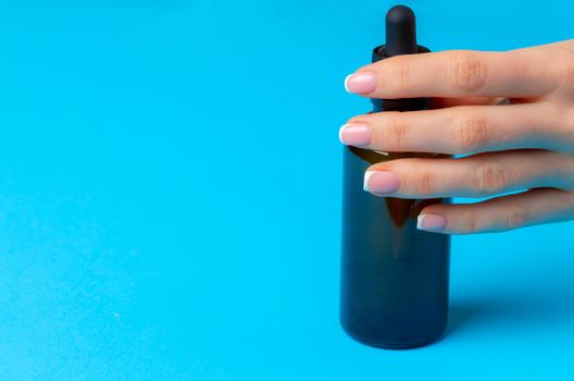 Female hand holding skincare product bottle on blue background