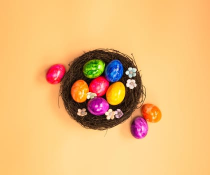 Colorful painted Easter Egg Nest with orange pastel colored background top view, Happy Easter Holliday concept background with Copy space spring bright colors design space for text